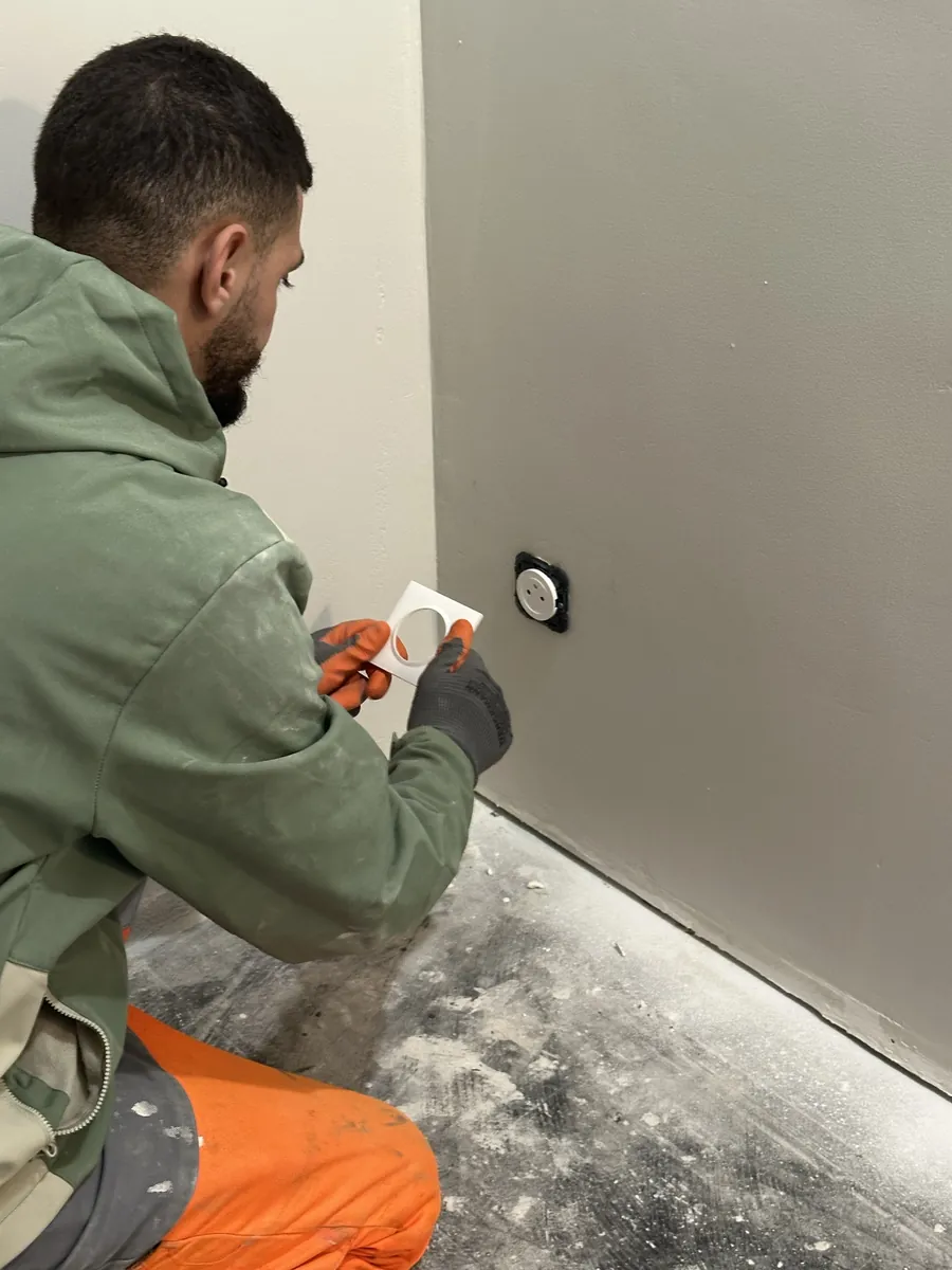 Électricien NYELEC posant la plaque de finition de la nouvelle prise de courant à Créteil